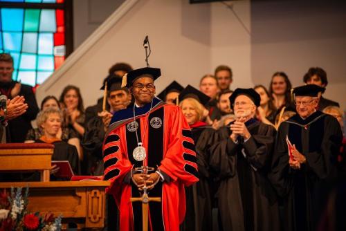 President Hayles smiles on stage and board members clap behind him.