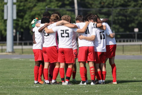 Men's soccer team huddles on the field.