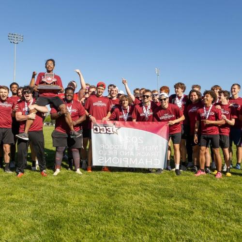 The men's track 和 field team smiles with 的ir championship  trophy 和 banner.